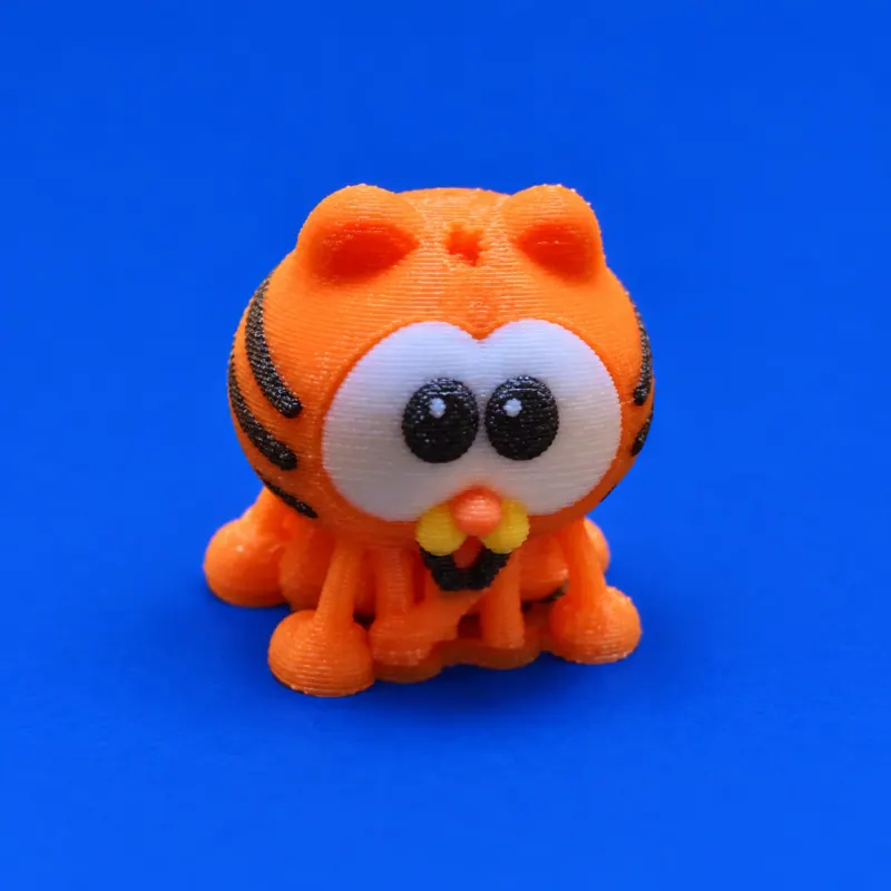 Uma miniatura Garfield bebê laranja sobre fundo azul, com olhos impressos brancos e pretos, focinho amarelo e camadas de impressão visíveis, sem ferragem
