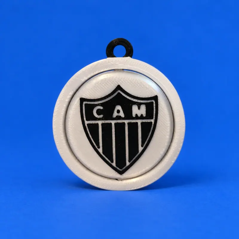 Chaveiro circular branco do Atlético Mineiro com escudo CAM preto e branco no disco giratório e elo preto integrado, apoiado sobre fundo azul