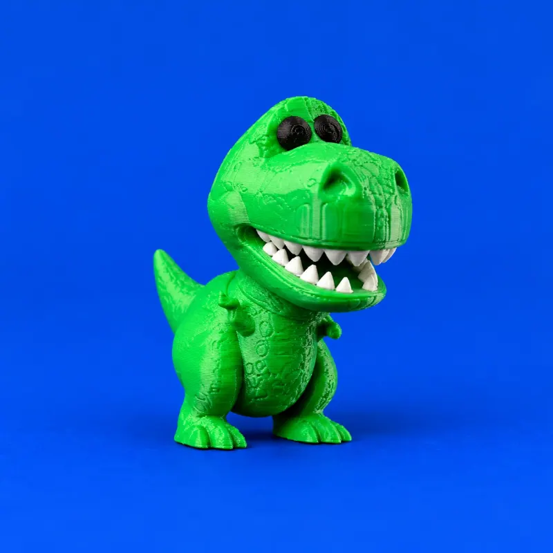 Uma miniatura Rex verde em fundo azul, com olhos pretos e dentes brancos impressos, dois pés apoiados e cauda única