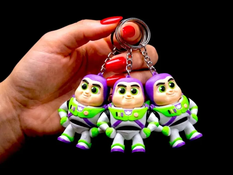 Três chaveiros Buzz presos a correntes e argolas na mão, com traje branco, verde e roxo, rosto em tom de pele e olhos impressos