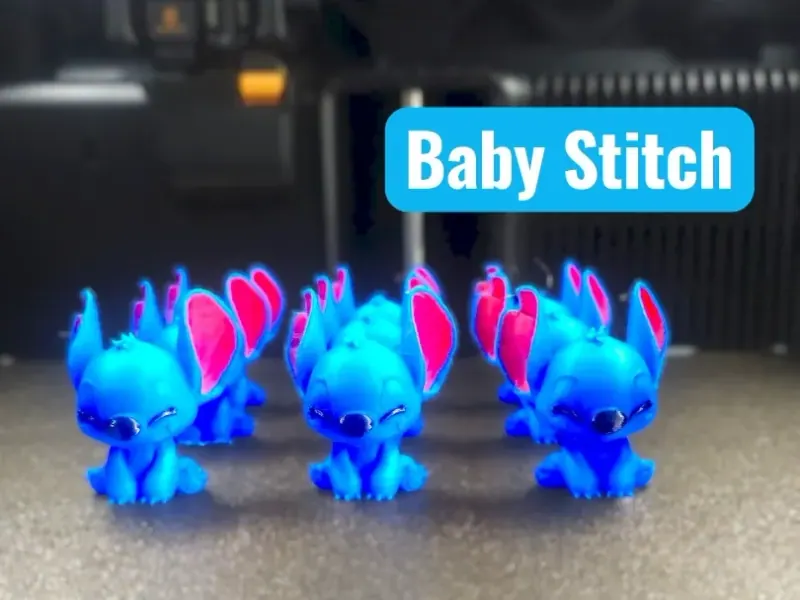 Lote de Baby Stitch sentado sobre mesa de impressão, corpo azul vivo, interior das orelhas rosa, nariz e olhos fechados azul-escuros impressos