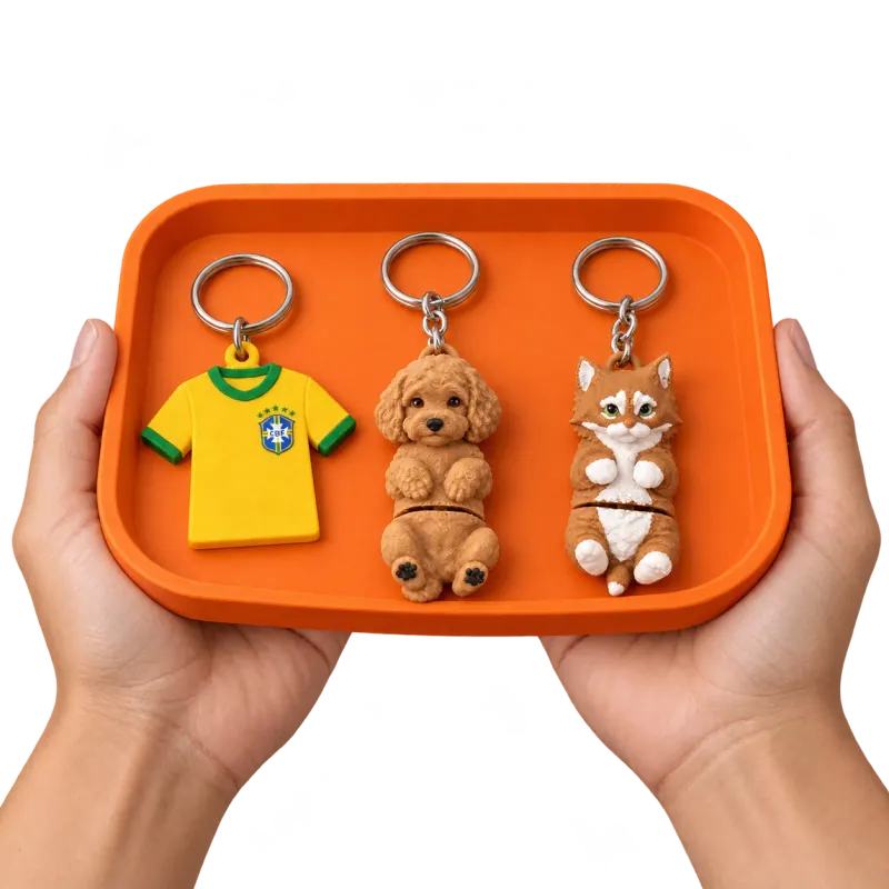 Mãos segurando uma bandeja laranja com chaveiros da Seleção Brasileira, um Maltipoo caramelo e um gato articulado